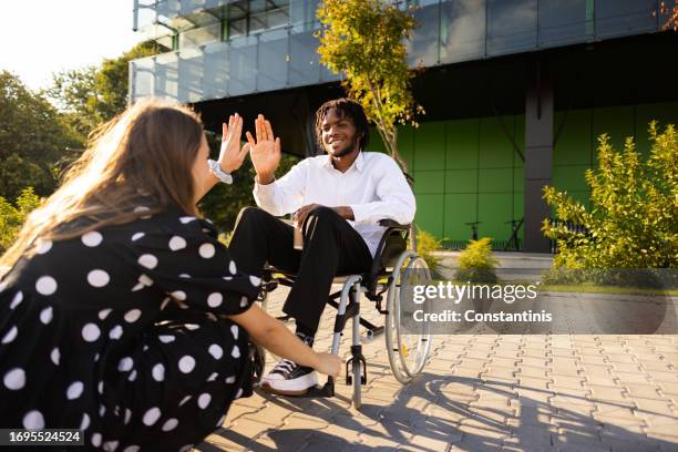 caucasian woman interchange high-five with an disabled young man of black ethnicity after she helped him to tie shoelace - high five interchange stock pictures, royalty-free photos & images