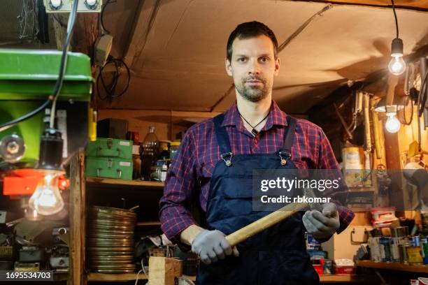 young carpenter in work overalls with hammer in retro workshop with work tools - handyman overalls stock pictures, royalty-free photos & images