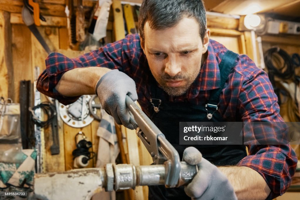 Adjustable wrench - worker unscrewing a water pipe in an old repair shop