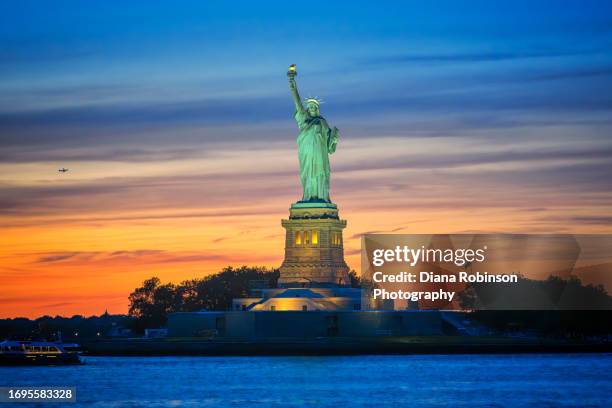 sunset behind the illuminated statue of liberty in new york harbor - statue of liberty in new york city stock pictures, royalty-free photos & images