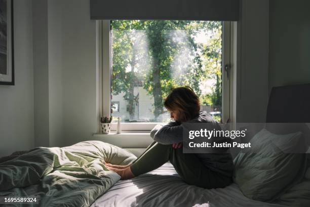 powerful image of a mature woman sitting on her bed - negative emotions - wonen stock pictures, royalty-free photos & images