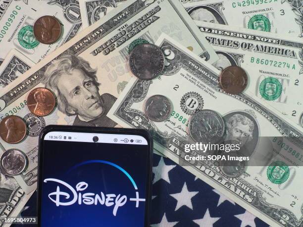 In this photo illustration, Disney+ logo seen displayed on a smartphone with United States Dollar notes and coins in the background.