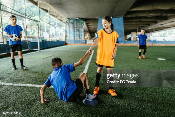 soccer girl player helping the adversary player to get up on the soccer field - gender equality sports stock pictures, royalty-free photos & images