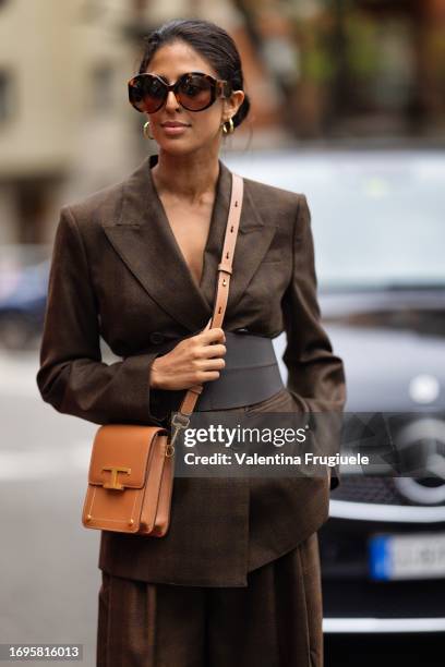 Guest is seen wearing Tod's brown sunglasses, gold hoop earrings, a brown leather belt, a Tod's leather cross-body beige bag and a checked brown suit...