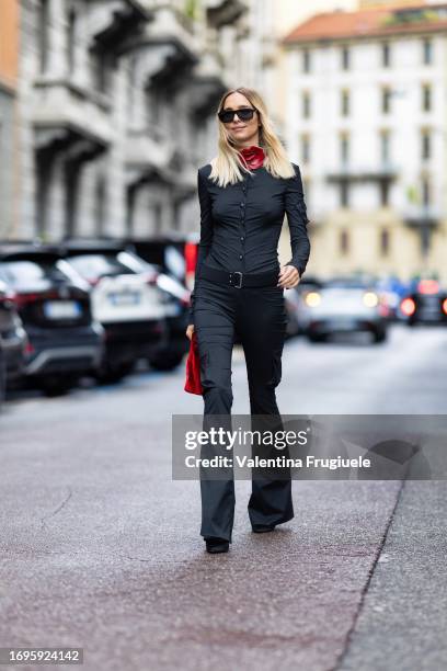 Candela Pellizza is seen wearing a grey shirt, a black belt, grey trousers, a red bag, black sunglasses and a red chocker with a 3d leather flower...