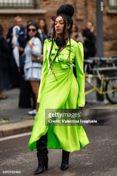 Coco Rebecca Edugamhe is seen wearing a chocker with a black 3d flower application, black leather boots and a fluorescent green long dress outside...