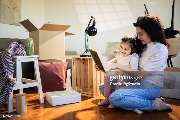 woman and her little daughter looking at the framed picture while moving in - belongings stock pictures, royalty-free photos & images