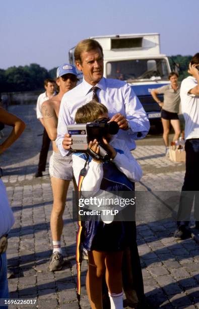 English actor Roger Moore , is James Bond, lets a young boy use a video camera during the filming of the 1985 James Bond spy movie, "A View to a...