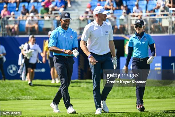 Former NFL player Victor Cruz, Garrett Hilbert of Dude Perfect and actress Kathryn Newton smile as they arrive on the first tee for the All Star...