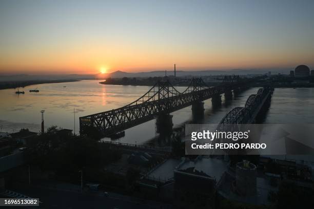 This photo taken on September 21, 2023 shows the sun rising behind the Friendship Bridge and Broken Bridge, which leads across the Yalu River into...