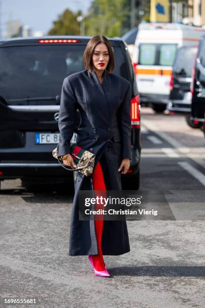 Tiffany Hsu wears navy tailored coat, bag with print, red stockings outside Gucci during the Milan Fashion Week - Womenswear Spring/Summer 2024 on...