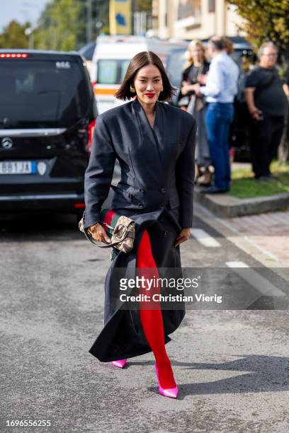 Tiffany Hsu wears navy tailored coat, bag with print, red stockings outside Gucci during the Milan Fashion Week - Womenswear Spring/Summer 2024 on...