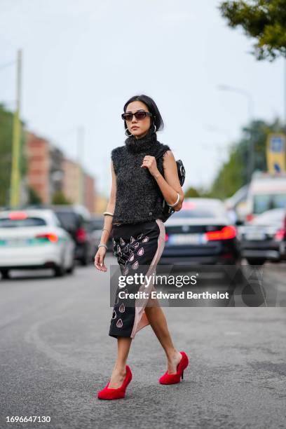 Yoyo Cao wears sunglasses, earrings, a midi skirt with printed drop-shaped patterns, red fluffy shoes, large bracelets around the forearms, outside...