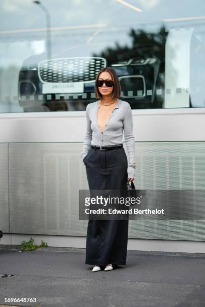 Aimee Song wears sunglasses, a golden necklace, a low-neck gray wool cardigan, a black leather belt, dark gray pants, pointed shoes, outside Gucci,...