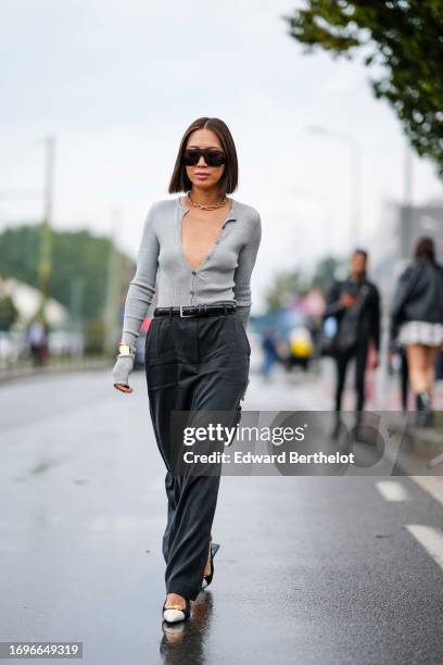 Aimee Song wears sunglasses, a golden necklace, a low-neck gray wool cardigan, a black leather belt, dark gray pants, pointed shoes, outside Gucci,...