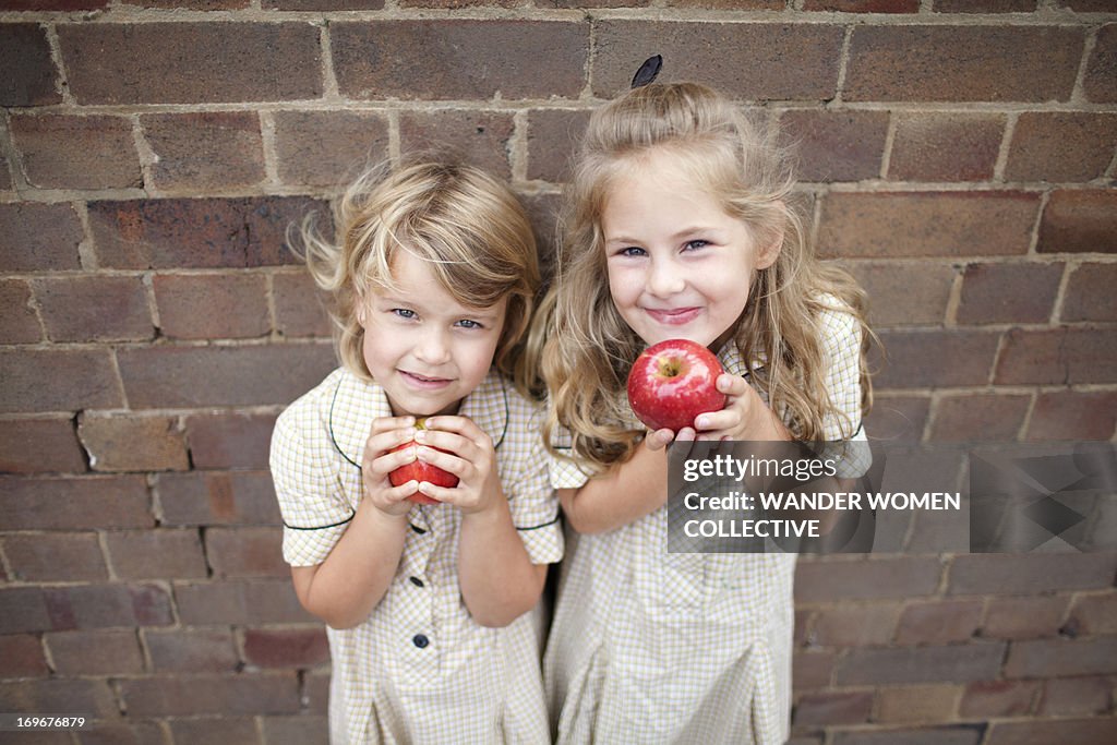Two young girls in school uniform eating apples