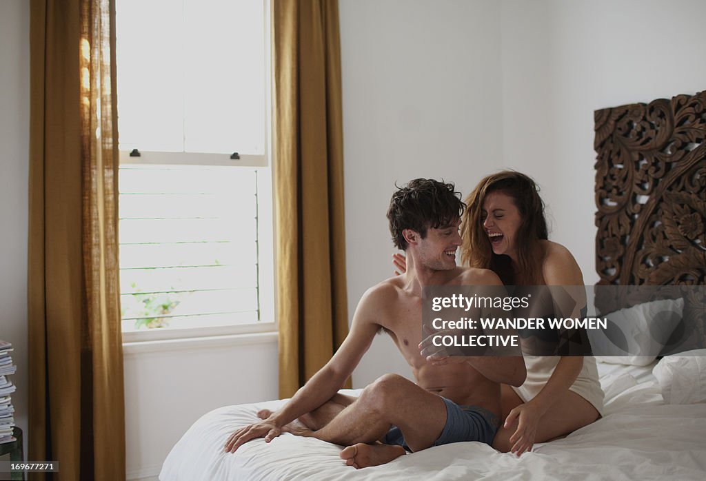 Couple sitting on bed cuddling and laughing