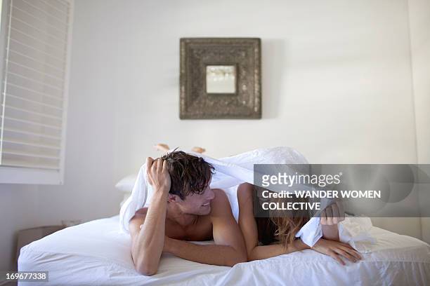 couple in bed hiding under white sheets - women being spanked photos et images de collection
