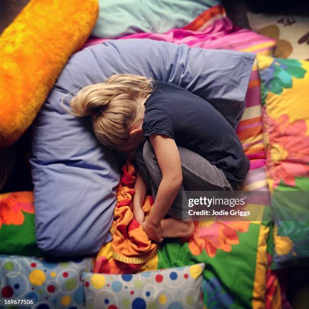 child curled up in ball on soft pile of cushions - love photos et images de collection