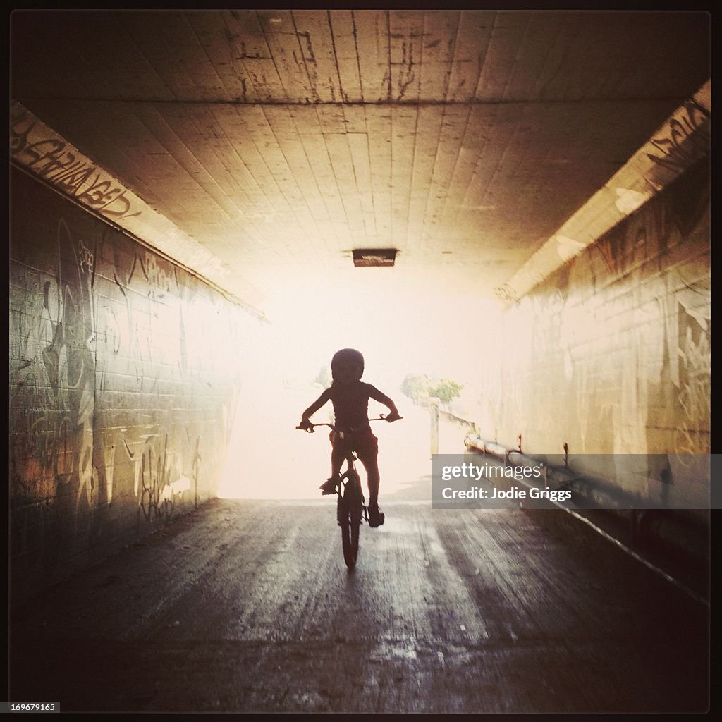 Silhouette of child riding bike through tunnel