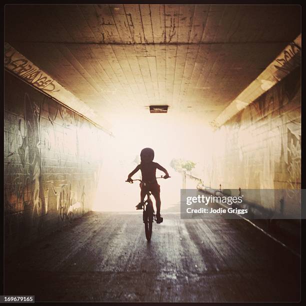 Silhouette of child riding bike through tunnel