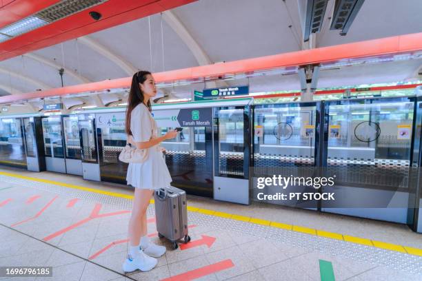 female tourist holding a credit card dragging her wallet waits for the subway at the mrt station. singapore - singapore mrt stock pictures, royalty-free photos & images