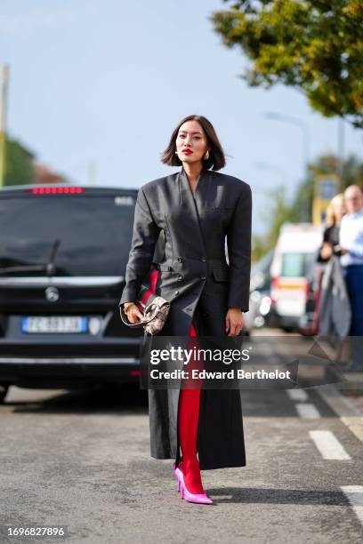 Tiffany Hsu wears a black long coat with shoulder pads, a Gucci monogram bag, red tights, pink pointed shoes, outside Gucci, during the Milan Fashion...