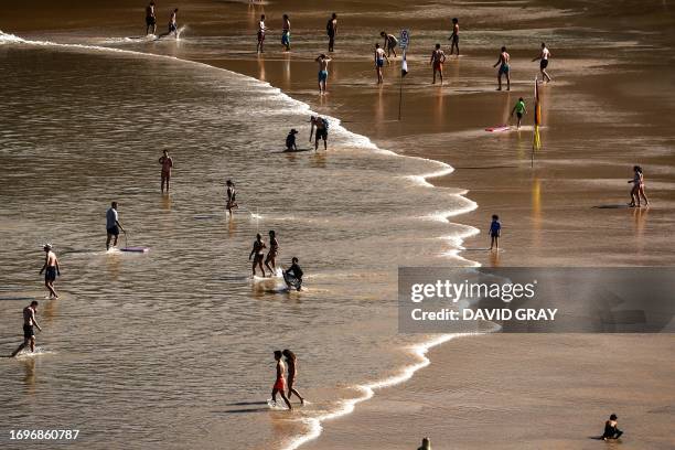 Beachgoers walk into the surf as others walk on Freshwater Beach, located in the northern beaches area of Sydney, on September 29, 2023.