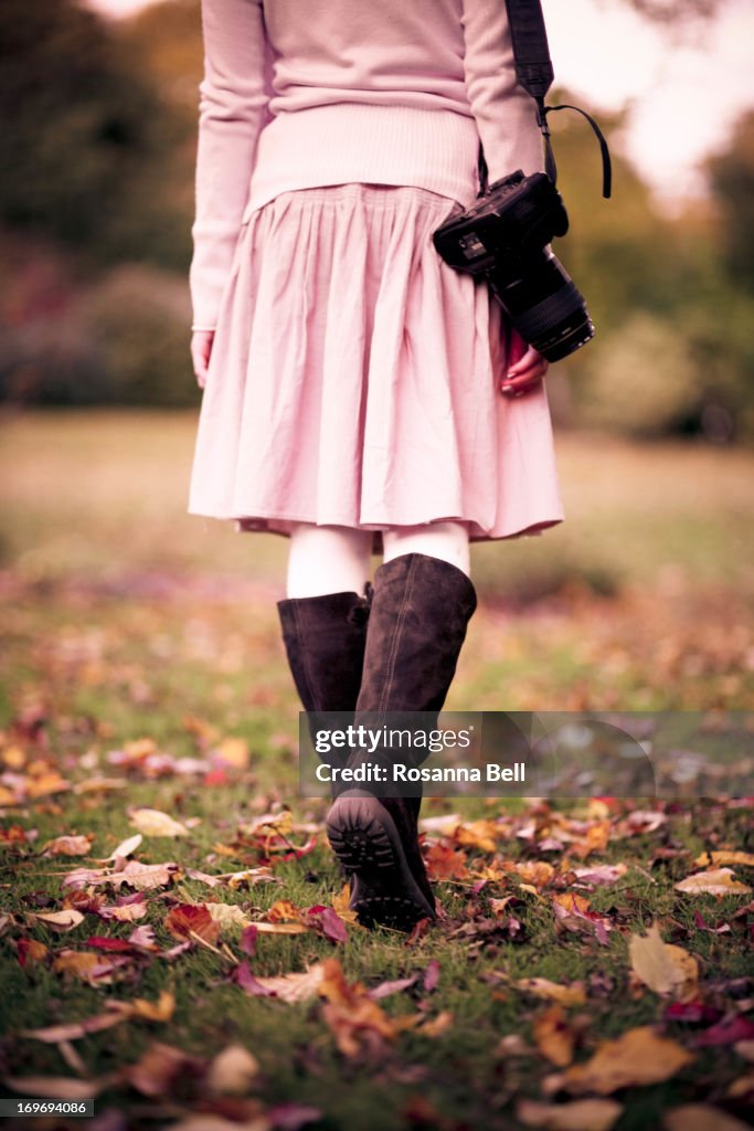 Girl walking away in autumn leaves with camera