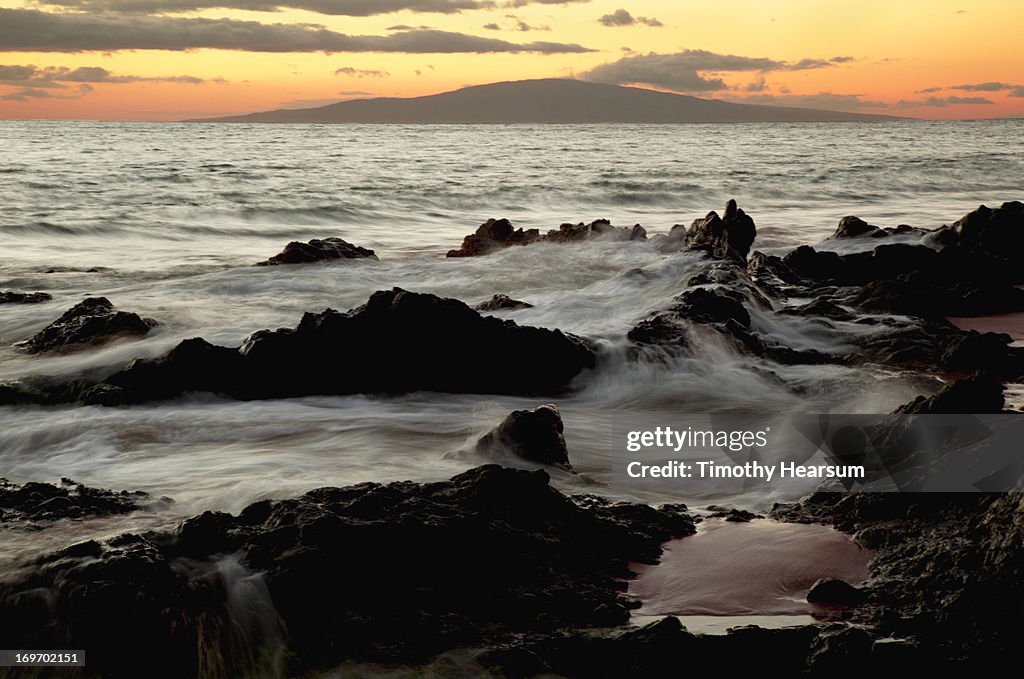 Waves washing over lava rock at sunset