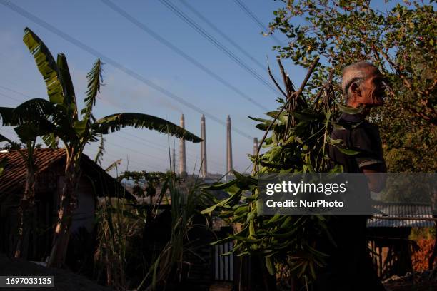 Villagers pass by on the village road as smoke ash spews from the chimney of the coal power plant owned by Indonesian Power in Cilegon, Banten...