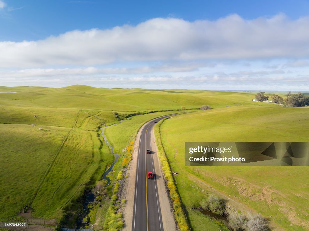 Aerial view of Car on the road going in the american countryside with cow farm, meadow, stream and mountain in background.
