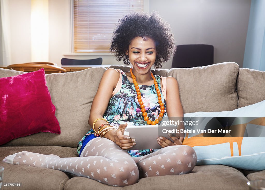 Young woman watching digital tablet in livingroom.