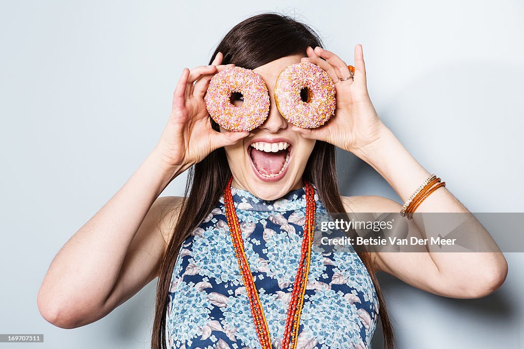 Woman holding doughnuts in front of eyes.