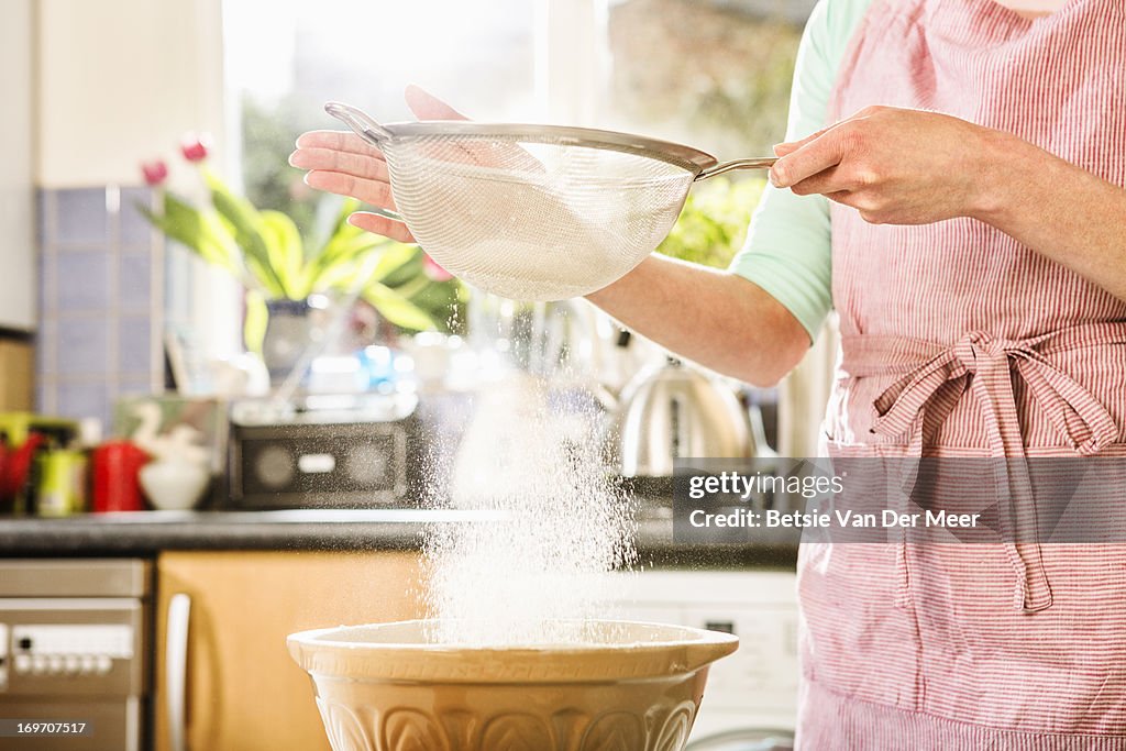 Sieving flour in bowl, close up.