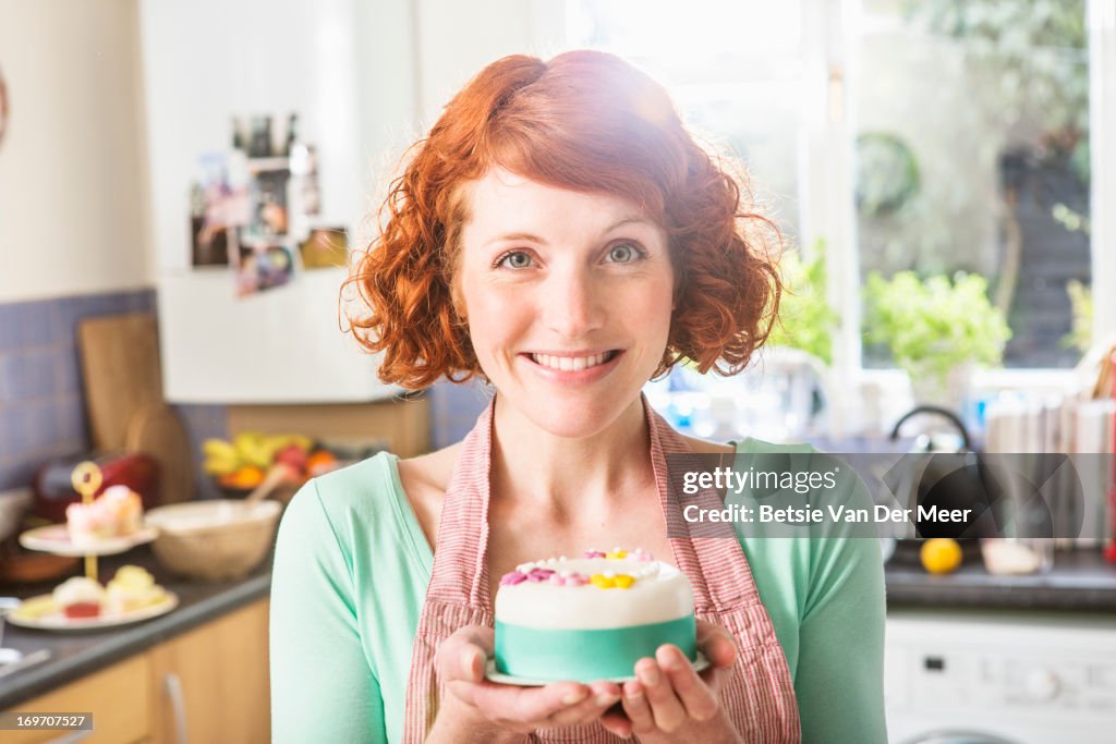 Woman holding decorated icing cake, in kitchen.