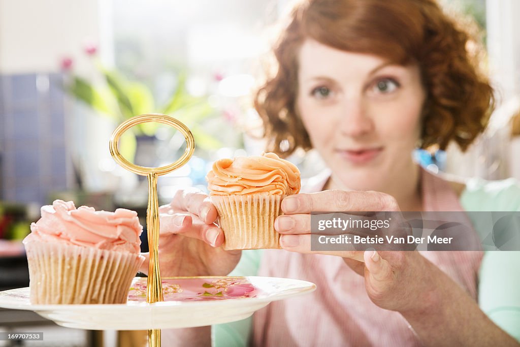 Woman places cupcake on cake plate.