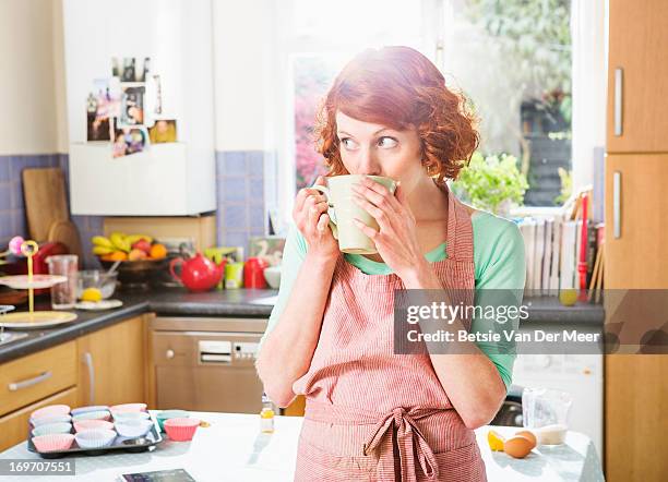 woman having a cup of tea while baking cupcakes. - tea and cupcakes stockfoto's en -beelden