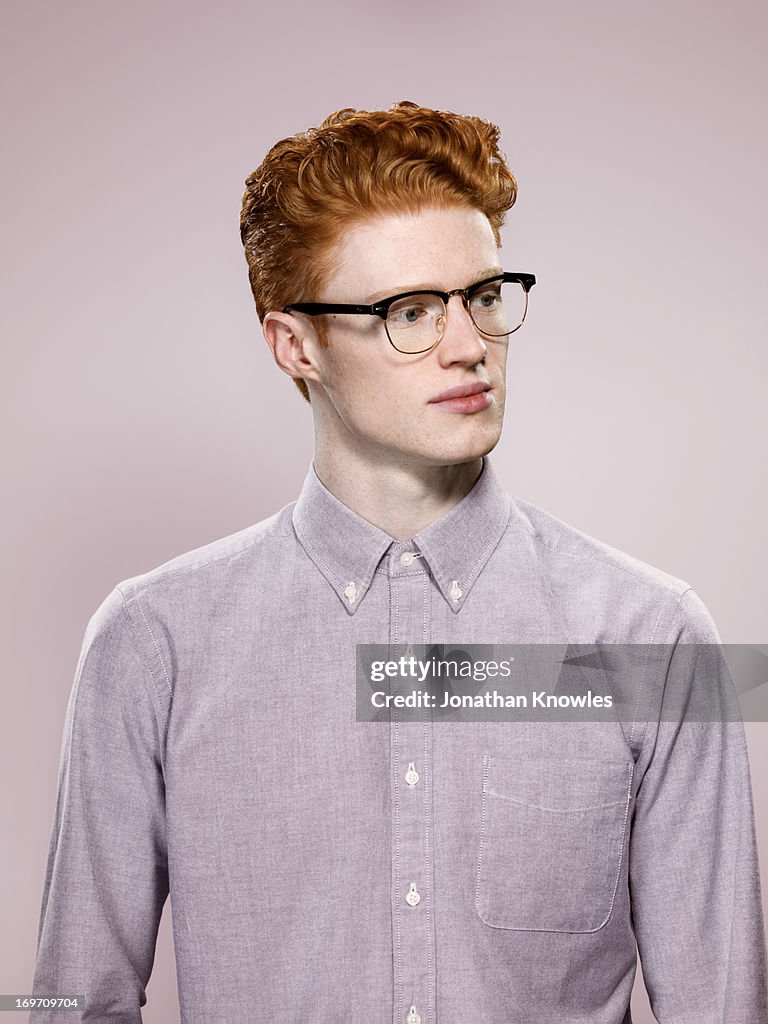 Male with wavy red hair and glasses, looking away