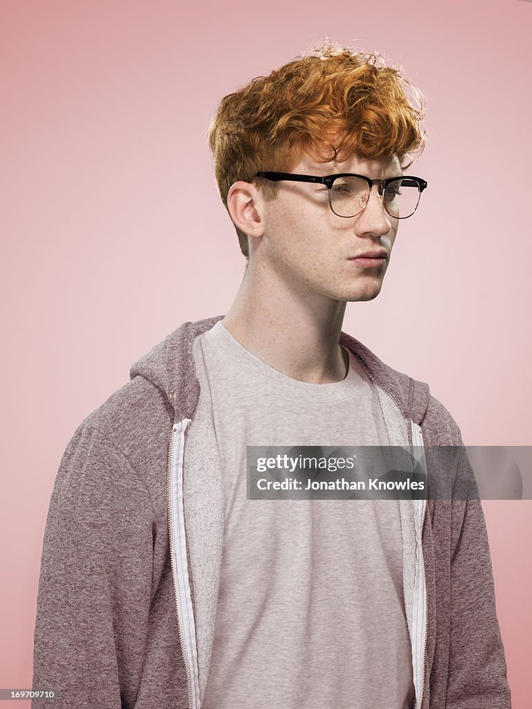 Male with curly red hair and glasses looking away