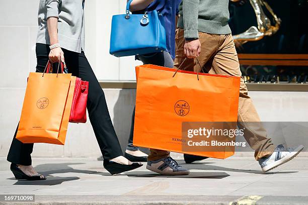 Pedestrians carry Hermes International SCA branded shopping bags as they walk along New Bond Street in London, U.K., on Friday, May 31, 2013. LVMH...