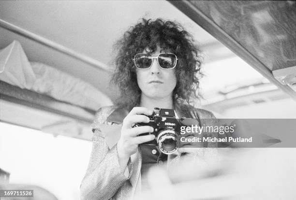 Singer Marc Bolan , of English glam rock group T-Rex, holding a Nikon camera on a tour bus during a four-date British tour, June 1972.