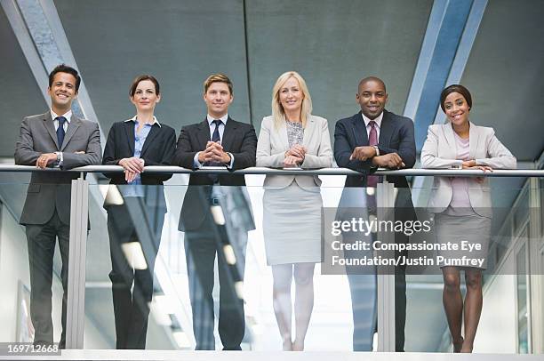 smiling business people standing on atrium balcony - group of businesspeople standing low angle view stock pictures, royalty-free photos & images