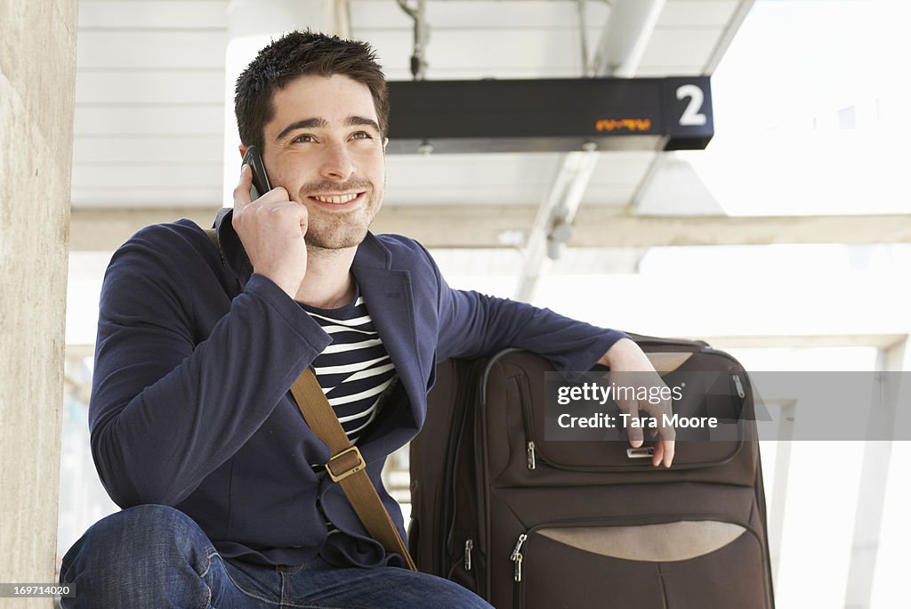 Man with suitcase and mobile at train station