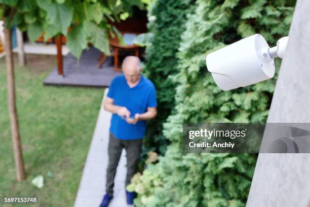 hombre mayor instalando cámara de seguridad para vigilancia doméstica - cámara de seguridad fotografías e imágenes de stock