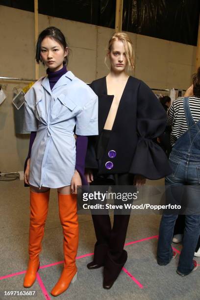 Backstage at the Jacquemus show during Paris Fashion Week Autumn/Winter 2016/17, one model wears a blue dress shirt cinched at the waist and orange...