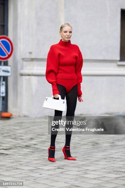 Leonie Hanne is seen wearing red Loewe sunglasses, silver earrings, black tights, red shiny pumps, a white leather Ferragamo bag, a red turtleneck...