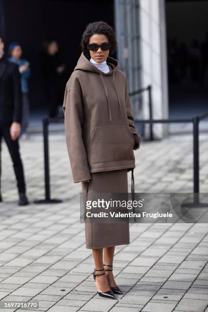 Tina Kunakey is seen wearing tortoiseshell Ferragamo sunglasses, black shiny pumps, a white turtle-neck sweater, a brown hoodie and the matching midi...