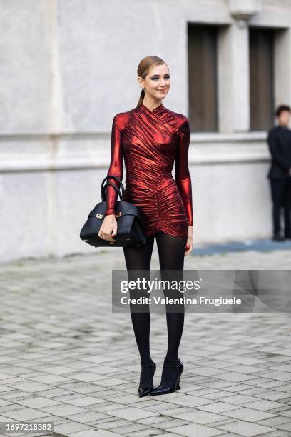 Chiara Ferragni is seen wearing blue eyeshadow, a red lycra long sleeves dress, black tights, black shiny pumps and a black leather Ferragamo bag...