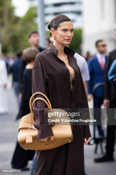 Bianca Balti is seen wearing gold hoop earrings, a light beige leather Ferragamo bag with gold hardware and a brown long shirt outside the Ferragamo...